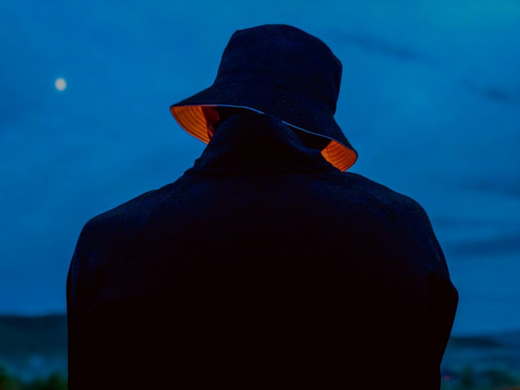 a man in a black jacket and a hat looking at the moon