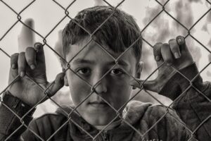 boy, fence, poverty, hungry, sad, desperate, poor, child, captivity, chain link, chain link fence, grid, conceptidea, young boy, portrait, boy portrait, monochrome, sad boy, black and white